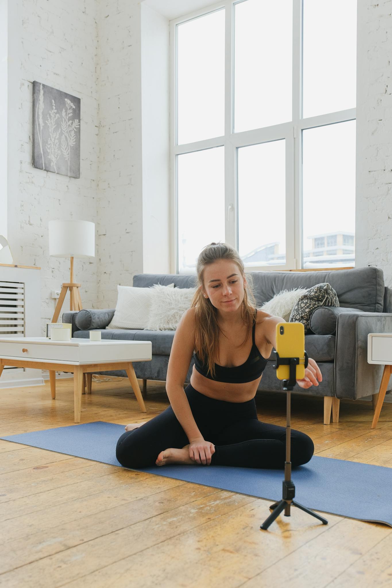 A woman in activewear films a yoga session at home using a smartphone.