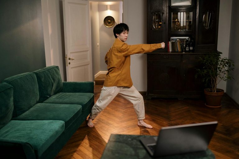 Adult practicing martial arts indoors, demonstrating skill and focus with a laptop nearby.