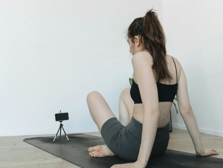 Woman doing yoga exercises at home, recorded on smartphone tripod for blogging content.