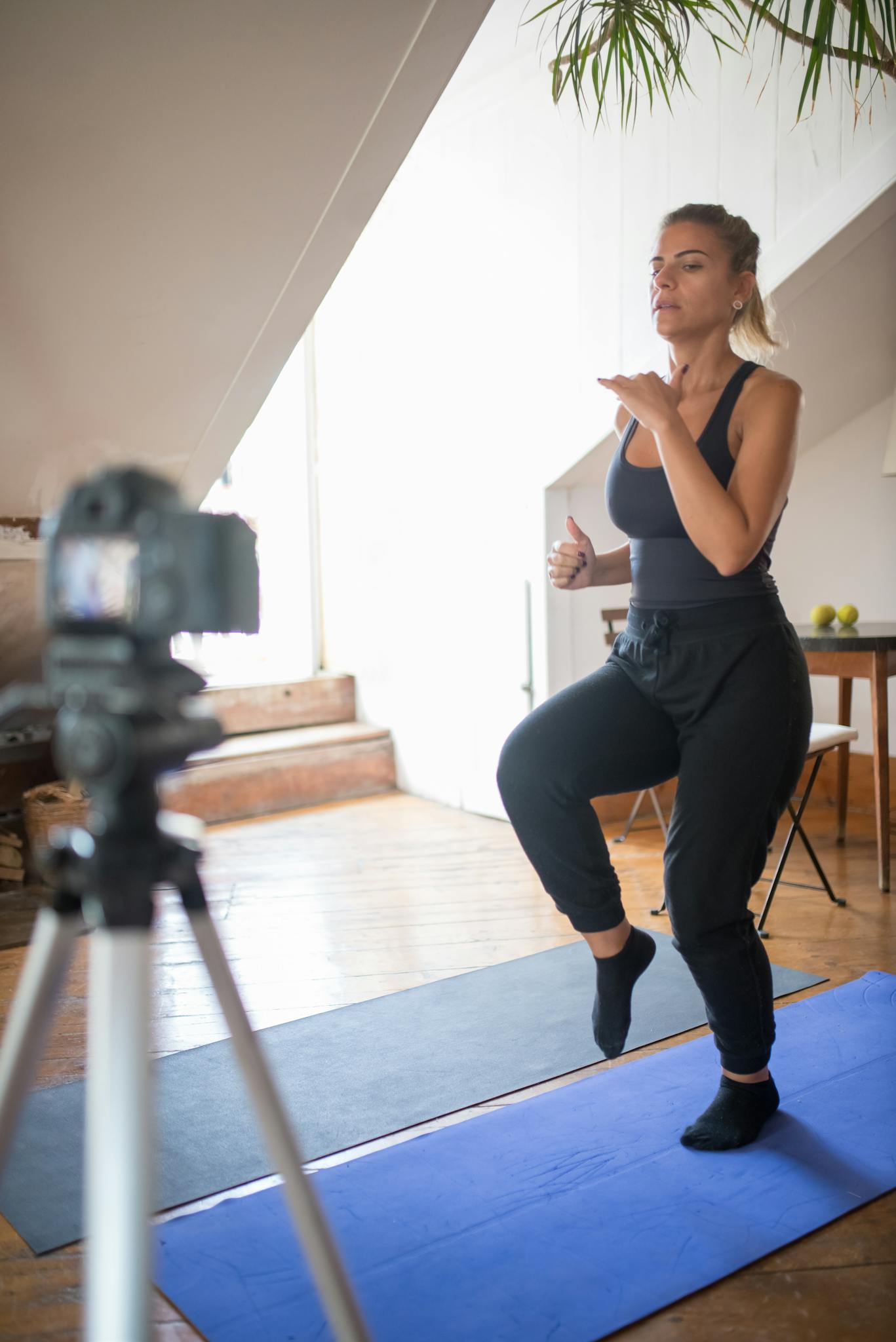 Woman performing exercises at home while recording an online workout video in a bright living room.
